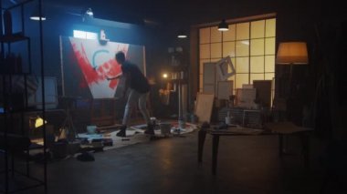 Yetenekli erkek ressam soyut bir resim üzerinde çalışıyor, Endüstriyel Roller 'ı kullanarak cesur duygusal bir modern resim çiziyor. Easel Aydınlatma Üzerine Karanlık Yaratıcı Stüdyo Büyük Tuval Standı. Yavaş Hareket