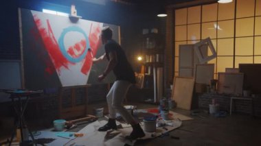 Yetenekli erkek ressam soyut bir resim üzerinde çalışıyor, Endüstriyel Roller 'ı kullanarak Cesur Duygusal Modern Resimler yaratıyor. Easel 'deki Karanlık Yaratıcı Stüdyo Büyük Tuval Stantları. Yavaş Hareket Büyüt