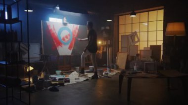 Yetenekli erkek ressam soyut bir resim üzerinde çalışıyor, Endüstriyel Roller 'ı kullanarak Cesur Duygusal Modern Resimler yaratıyor. Karanlık Yaratıcı Stüdyo, Büyük Tuvaller Easel 'de Duruyor