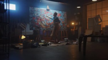 Yetenekli Kadın Sanatçı Soyut Yağlıboya Üzerine Çalışıyor, Boya Fırçası Kullanarak Modern Başyapıt ı Yaratıyor. Koyu ve Dağınık Yaratıcı Stüdyo nerede Büyük Tuval Easel Işıklı duruyor. Dolly Atış