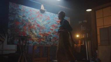 Yetenekli Kadın Sanatçı Soyut Yağlıboya Üzerine Çalışıyor, Boya Fırçası Kullanarak Modern Başyapıt ı Yaratıyor. Koyu ve Dağınık Yaratıcı Stüdyo nerede Büyük Tuval Easel Işıklı Standları