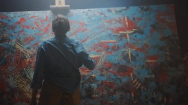 Yetenekli Kadın Sanatçı Enerjik ve Hevesle Boya Fırçası Kullanarak O Yağlıboya Modern Masterpiece oluşturur. Çarpıcı Renkler Büyük Tuval ile Yaratıcı Stüdyo. Düşük ve Eğim Açısı Atış