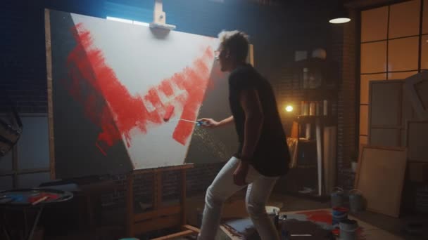 Талантливый мужчина-художник, работающий над абстрактной живописью, использует промышленный ролик, чтобы рисовать смело эмоциональную современную картину. Dark Creative Studio Large Canada Stands on Easel Illuminated. Slow Motion — стоковое видео