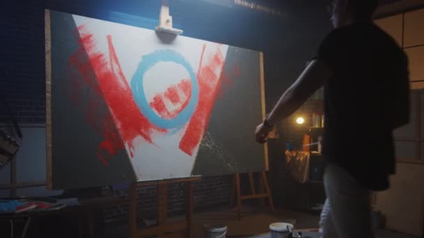 Artista masculino talentoso trabalhando em uma pintura abstrata, usa rolo industrial para criar imagem moderna Daringly Emotional. Estúdio criativo escuro, grande lona fica no cavalete. Lento movimento Zoom para fora — Vídeo de Stock