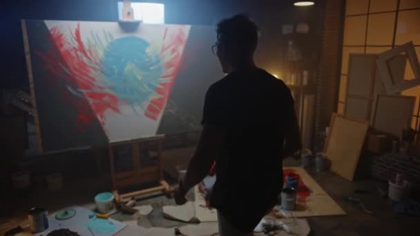 Artista talentoso que trabaja en la pintura abstracta, utiliza el rodillo de pintura para crear una imagen moderna audazmente emocional. Dark Creative Studio Lona grande se destaca en el caballete iluminado. Slow Motion siguiente disparo — Vídeos de Stock