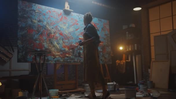 Utalentowana kobieta artysta pracuje na abstrakcyjne malowanie olejowe, za pomocą farby Pędzel tworzy Modern arcydzieło. Ciemne i brudne Studio kreatywne, gdzie duży płótno stoi na Easel podświetlane. Niski kąt — Wideo stockowe