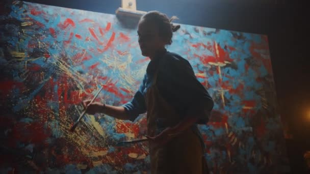ペイントブラシを使った才能あふれる女性アーティスト、油絵の現代傑作を生み出す。大きなキャンバスがイーゼルに立つクリエイティブスタジオ。ローアングルフォローショット — ストック動画