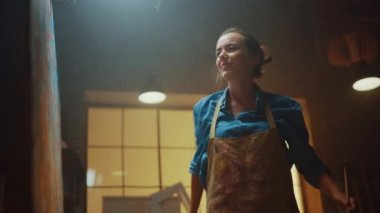 Modern Soyut Yağlıboya Üzerinde Çalışan Yetenekli Kadın Sanatçının Portresi, Boya Fırçası Kullanarak Geniş Vuruşlarla Gesturing. Dark Creative Studio Büyük Resim Easel Işıklı duruyor. Düşük Açı