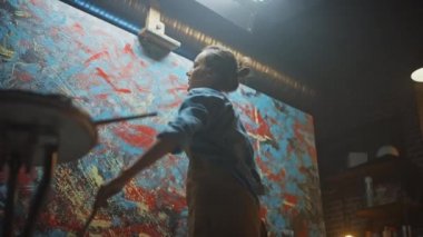 Kadın Sanatçı Soyut Yağlıboya Üzerine Çalışıyor, Hareketli Boya Fırçası Enerjik Olarak Modern Başyapıt ı Yaratıyor. Koyu ve Dağınık Yaratıcı Stüdyo nerede Büyük Tuval Easel Işıklı duruyor. Düşük Açı