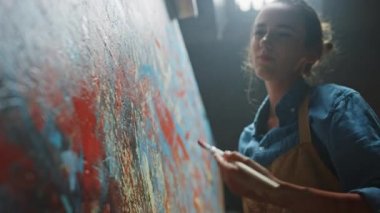 Kadın Sanatçı Soyut Yağlıboya Üzerine Çalışıyor, Hareketli Boya Fırçası Enerjik Olarak Modern Başyapıt ı Yaratıyor. Koyu Yaratıcı Stüdyo nerede Büyük Tuval Easel Işıklı duruyor. Düşük Açı Yakın çekim