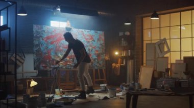 Yetenekli Erkek Sanatçı Enerjik ve Şiddetle Boya Fırçası Kullanarak O Yağlıboya Modern Masterpiece oluşturur. Çarpıcı Renklerin Büyük Tuvali ile Karanlık ve Dağınık Yaratıcı Stüdyo