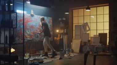 Yetenekli Erkek Sanatçı Enerjik ve Şiddetle Boya Fırçası Kullanarak O Yağlıboya Modern Masterpiece oluşturur. Çarpıcı Renklerin Büyük Tuvali ile Karanlık ve Dağınık Yaratıcı Stüdyo