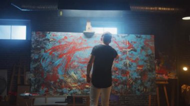 Yetenekli Erkek Sanatçı Enerjik ve Şiddetle Boya Fırçası Kullanarak O Yağlıboya Modern Masterpiece oluşturur. Çarpıcı Renkler Büyük Tuval ile Yaratıcı Stüdyo. Çekimden Sonra Geri Görünüm