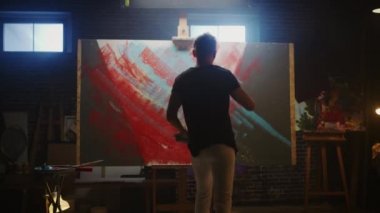 Yetenekli Erkek Sanatçı Soyut Bir Resim Üzerinde Çalışıyor, Cesurca Duygusal Modern Resim Oluşturmak için Endüstriyel Roller kullanır. Dark Creative Studio Büyük Tuval Easel Işıklı Standları