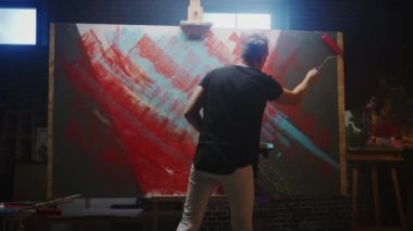 Yetenekli Erkek Sanatçı Soyut Bir Resim Üzerinde Çalışıyor, Cesurca Duygusal Modern Resim Oluşturmak için Endüstriyel Roller kullanır. Dark Creative Studio Büyük Tuval Easel Işıklı Standları