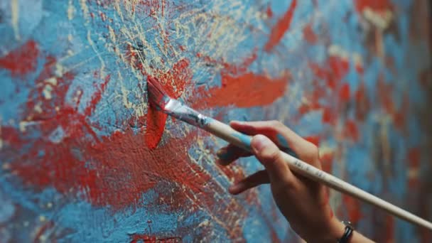 女性アーティストハンドのクローズアップショット、ペイントブラシを持ち、赤いペイントで絵を描く。カラフルでエモーショナルな油絵。現代の抽象美術作品を生み出す現代画家 — ストック動画
