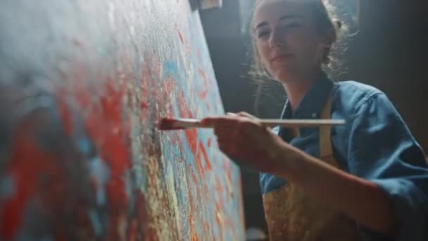 Female Artist Works on Abstract Oil Painting, Moving Paint Brush Energetically She Creates Modern Masterpiece. Dark Creative Studio where Large Canvas Stands on Easel Illuminated. Low Angle Close-up — Stock Video