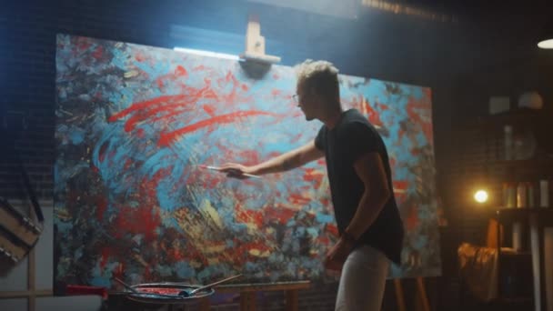 Talented Male Artist Energetically and Violently Using Paint Brush She Creates Modern Masterpiece of the Oil Painting. Dark and Messy Creative Studio with Large Canvas of Striking Colors — Stock Video