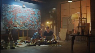 Stüdyolarında Oturan Birkaç Sanatçı Dizüstü Bilgisayar Kullanıyor, Bir Proje Üzerinde Çalışıyor, Konuşuyor ve Gülümsüyor. Ressam ve Ortağı Araştırma Yapıyor. Yağlıboya Resim ve Aletlerle Otantik Atölye