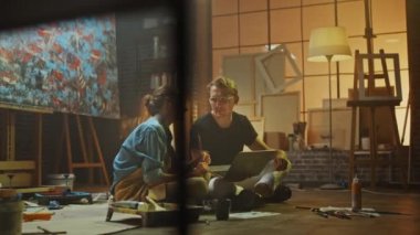 Stüdyolarında Oturan Birkaç Sanatçı Dizüstü Bilgisayar Kullanıyor, Bir Proje Üzerinde Çalışıyor, Konuşuyor ve Gülümsüyor. Ressam ve Ortağı Araştırma Yapıyor. Yağlıboya Resim ve Aletlerle Otantik Atölye