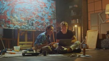 Stüdyolarında Oturan Birkaç Sanatçı Dizüstü Bilgisayar Kullanıyor, Bir Proje Üzerinde Çalışıyor, Konuşuyor ve Gülümsüyor. Ressam ve Ortağı Araştırma Yapıyor. Yağlıboya Resim ve Aletlerle Otantik Atölye