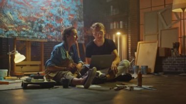 Stüdyolarında Oturan Birkaç Sanatçı Dizüstü Bilgisayar Kullanıyor, Bir Proje Üzerinde Çalışıyor, Konuşuyor ve Gülümsüyor. Ressam ve Ortağı Araştırma Yapıyor. Yağlıboya Resim ve Aletlerle Otantik Atölye