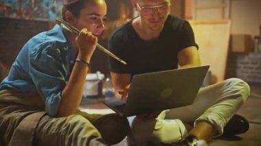 Stüdyolarında Oturan Birkaç Sanatçı Dizüstü Bilgisayar Kullanıyor, Bir Proje Üzerinde Çalışıyor, Konuşuyor ve Gülümsüyor. Ressam ve Ortağı Araştırma Yapıyor. Yağlıboya Resim ve Aletlerle Otantik Atölye