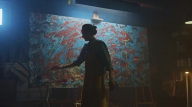 Kendine güvenen ve Kararlı Kadın Sanatçı Tuval için Walks ve Modern Soyut Yağlıboya Resim Başlar. Yaratıcı Studio Büyük Resim Easel Işıklı duruyor. Geri Görünüm Çekimini Takip Edin