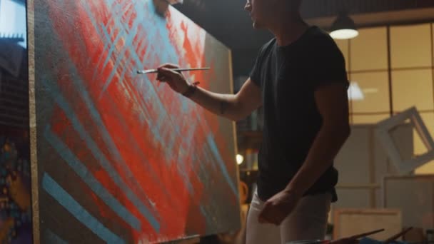 Tehetséges férfi művész energikusan és hevesen döntetlen a Paint Brush, ő teremti meg a modern Masterpiece az olajfestmény. Creative Studio, nagy vászon a feltűnő színek. Vissza megtekintése után shot — Stock videók