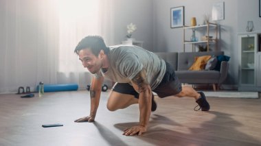 T-shirt ve Şort Güçlü Athletic Fit Man Onun Telefon bir Kronometre kullanırken Dağcı Egzersizleri yapıyor. O Minimalist İç ile Onun Geniş Daire Evde Eğitim.