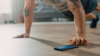 Push Up Egzersizleri Yapmadan Önce Telefonunda Kronometre Kullanarak T-shirt ve Şort bir Muscular Fit Man Close Up Shot. O Minimalist İç ile Dairesinde Evde Eğitim.