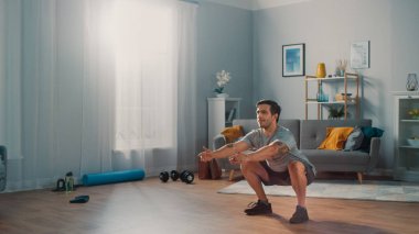 T-shirt ve Şort Kas Athletic Fit Man Minimalist İç ile Onun Geniş ve Parlak Daire Evde Squat Egzersizleri yapıyor.