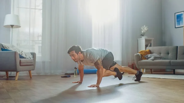 Muscular Athletic Fit Man in T-shirt and Shorts Energetically Starts Doing Mountain Climber Exercises at Home in His Spacious and Bright Apartment with Modern Interior.