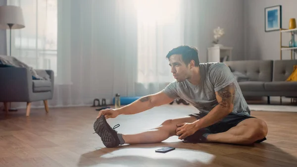 Forte Atlético Fit Man em T-shirt e Shorts Alonga seu corpo para exercícios matinais em casa em sua espaçosa e brilhante sala de estar com interior minimalista . — Fotografia de Stock