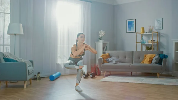 Hermosa chica fuerte de la aptitud en un top atlético está haciendo ejercicios de yoga del equilibrio en su sala de estar brillante y espaciosa con interior minimalista . — Foto de Stock