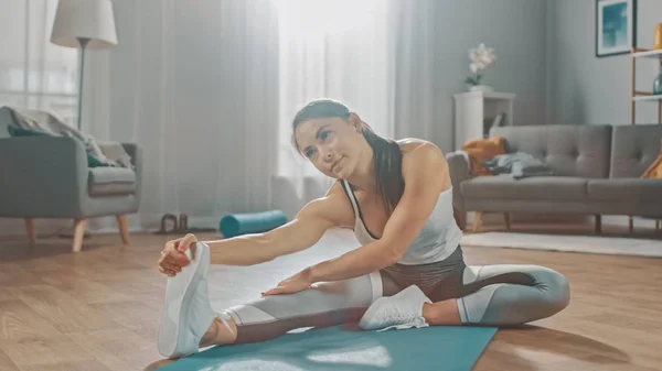 Hermosa chica de fitness segura en una ropa de entrenamiento atlético está haciendo ejercicios de yoga de estiramiento en su luminoso y espacioso salón con acogedor interior moderno . —  Fotos de Stock