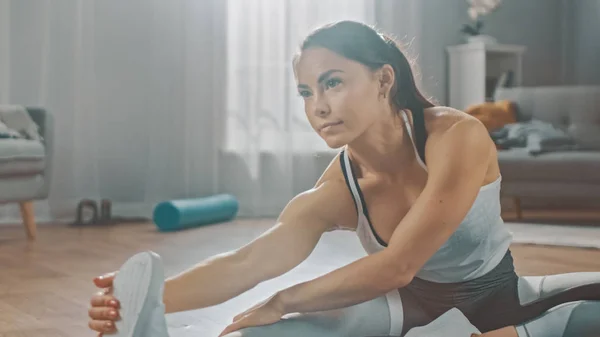 Bela garota de fitness confiante em uma roupa de treino atlético está fazendo exercícios de Yoga de alongamento em sua brilhante e espaçosa sala de estar com interior minimalista acolhedor . — Fotografia de Stock