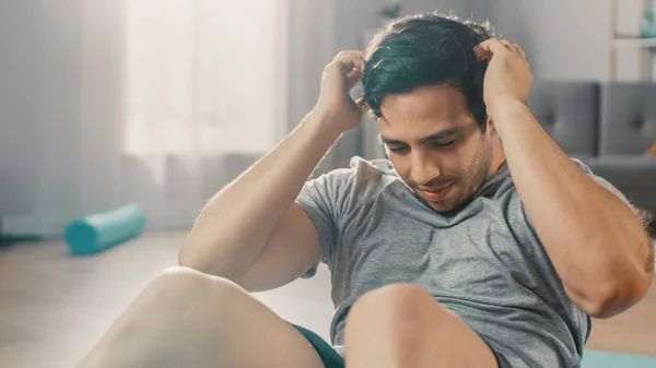 Strong Athletic Fit Man in T-shirt and Shorts is doing Abdominal Crunch Workout at Home in His Spacious and Bright Living Room with Minimalistic Interior. — Stock fotografie