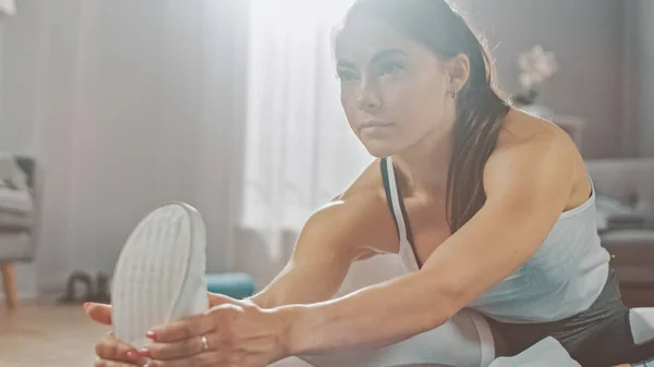 Bela garota de fitness confiante em uma roupa de treino atlético está fazendo exercícios de Yoga de alongamento em sua brilhante e espaçosa sala de estar com interior minimalista acolhedor . — Fotografia de Stock