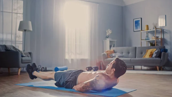 Forte atlético Shirtless Fit Man em calções cinza está fazendo exercícios abdominais em casa em sua espaçosa e ensolarada sala de estar com interior minimalista . — Fotografia de Stock