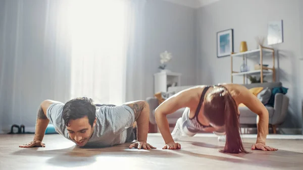 Shot μια ισχυρή και όμορφη αθλητική Fitness ζευγάρι στην προπόνηση ρούχα κάνει push up ασκήσεις. Φωτεινό και ευρύχωρο σαλόνι με μινιμαλιστικό εσωτερικό. — Φωτογραφία Αρχείου
