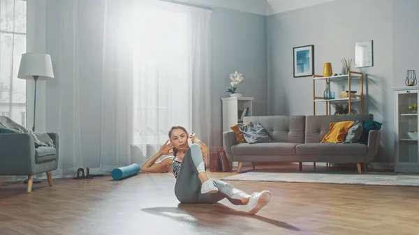 Starke und fitte schöne Mädchen in einem grauen athletischen Outfit energisch in ihrem hellen und geräumigen Wohnzimmer mit minimalistischem Interieur. — Stockfoto