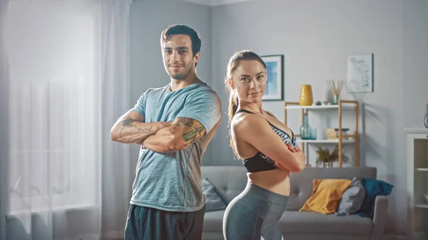 Homme athlétique musculaire et belle femme de remise en forme en vêtements d'entraînement posent avec confiance dans leur appartement lumineux et spacieux avec intérieur minimaliste . — Photo