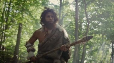 Tarih öncesi ormanda Hayvan Derisi Giyen İlkel Mağara Adamı 'nın Portresi ve Taş Ucu Mızrakla Kürk Avı. Tarih öncesi Neandertal Avcısı Ormanda İlkel Aletlerle Çöpleri Arıyor