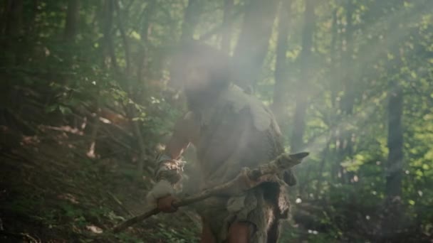 Retrato del cavernícola primitivo con piel de animal y piel de caza con una lanza de punta de piedra en el bosque prehistórico. Prehistórico Neanderthal Hunter listo para lanzar lanza en la selva — Vídeo de stock