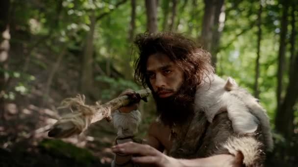 Primer plano Retrato del cavernícola primitivo con piel de animal y piel de caza con una lanza de punta de piedra en el bosque prehistórico. Prehistórico Neanderthal Hunter listo para lanzar lanza en la selva — Vídeo de stock