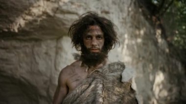 Hayvan derisi tutan ilkel mağara adamı portresi uçlu çekiç. Tarih öncesi Neandertal Avcı Pozisyonu Ormanda İlkel Avcılık. Kameraya Bakma