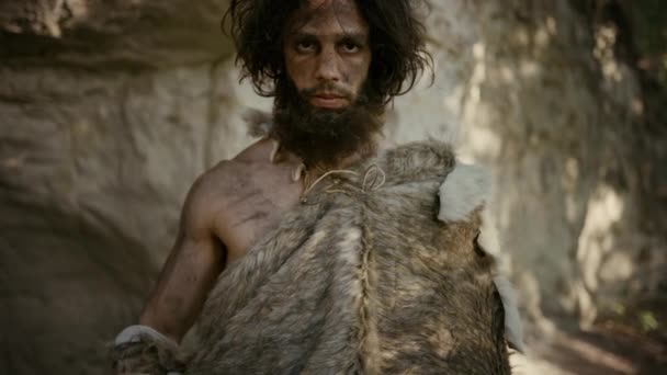 Ősi ősember portréja, aki állati bőrt visel, kő hegyű kalapács. Őskori neandervölgyi vadász pózol primitív vadászattal a dzsungelben. Nézem a kamerát. — Stock videók