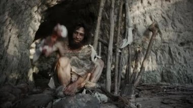 Hayvan derisi giyen ilkel mağara adamı kemik tutuyor ve onunla kayaya çarpıyor. Mağara girişinin yakınında Neandertal Ahmaklığı belki de ilk İlkel Aletler ya da Silahlar Kazayla Yaratılıyor.