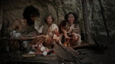 Tarih öncesi avcı-toplayıcı kabilesi Hayvan Derisi Giyen Gece Bir Mağarada Yaşıyor. Neanderthal ya da Homo Sapiens Ailesi Şenlik Ateşi 'nde Isınmaya Çalışıyor, Ateşin Üzerinde Elele tutuşuyor, Yemek Pişiriyor